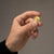 A man's hand holding the Bandor Coin, a solid 18k gold collectible coin struck with the founding ape, between thumb and forefinger. Luxury gold coin jewelry from the Bandorverse.