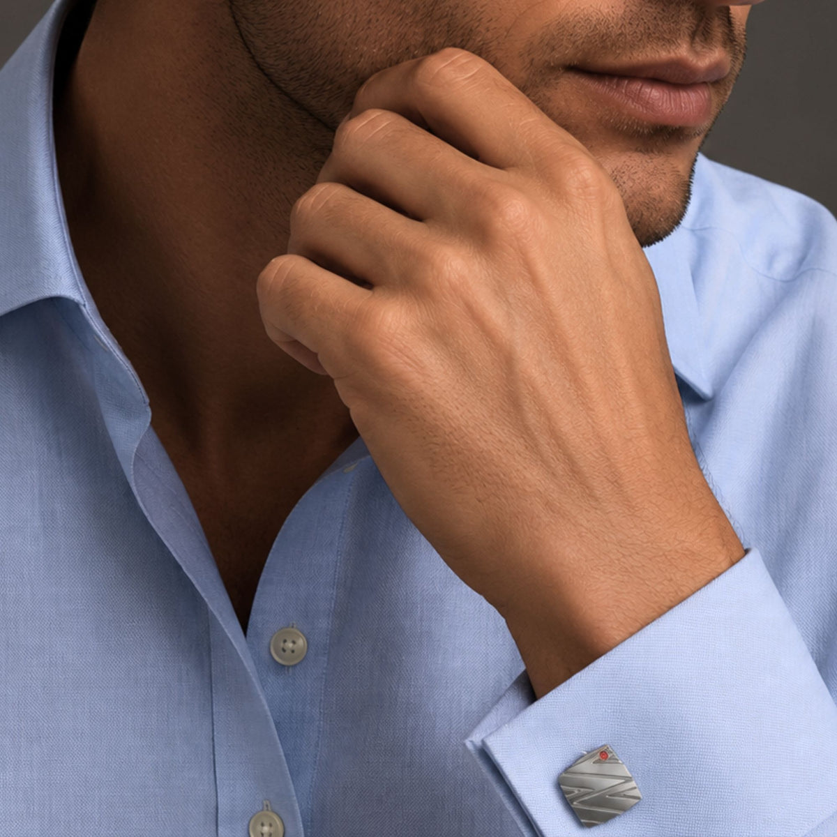 Man in a pale blue shirt wearing the Bandor Essence Cufflinks in platinum, hand raised to his jaw