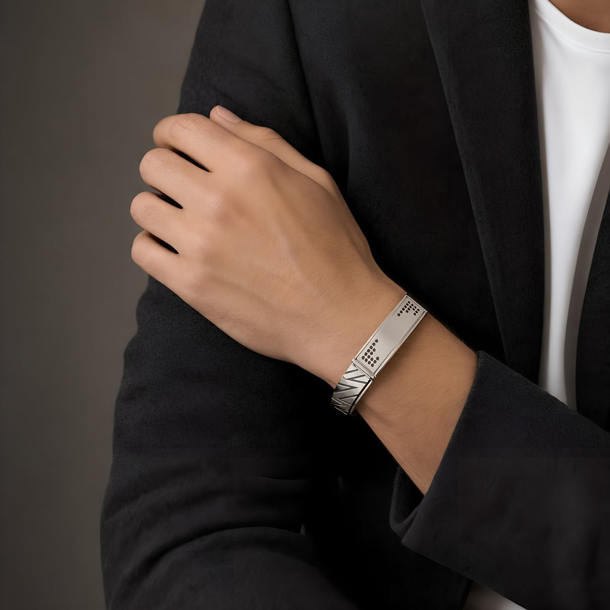 Man in a charcoal blazer wearing the Bandor Vanguard Cuff, a solid platinum cuff bracelet for men set with 32 natural black diamonds, the pave plaque visible on the wrist.