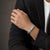 Man in a charcoal blazer wearing the Bandor Vanguard Cuff, a solid platinum cuff bracelet for men set with 32 natural black diamonds, the pave plaque visible on the wrist.